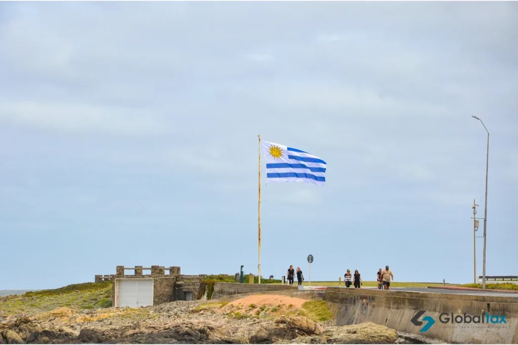 Bandeira uruguaia na orla com pessoas caminhando à beira-mar
